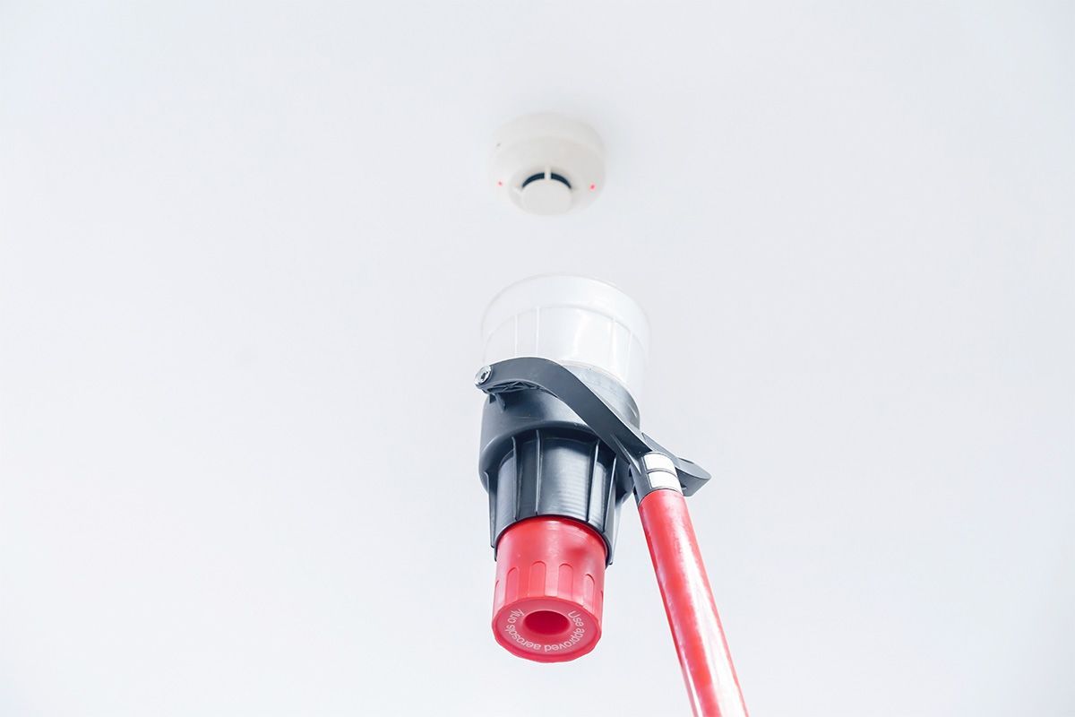Automatic smoke detector fire alarm head on the ceiling. The smoke detector is triggered by a small amount of aerosol smoke, the red indicator lights up